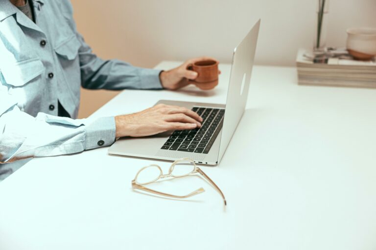 Casual workspace featuring laptop, coffee cup, and eyeglasses on a white table.